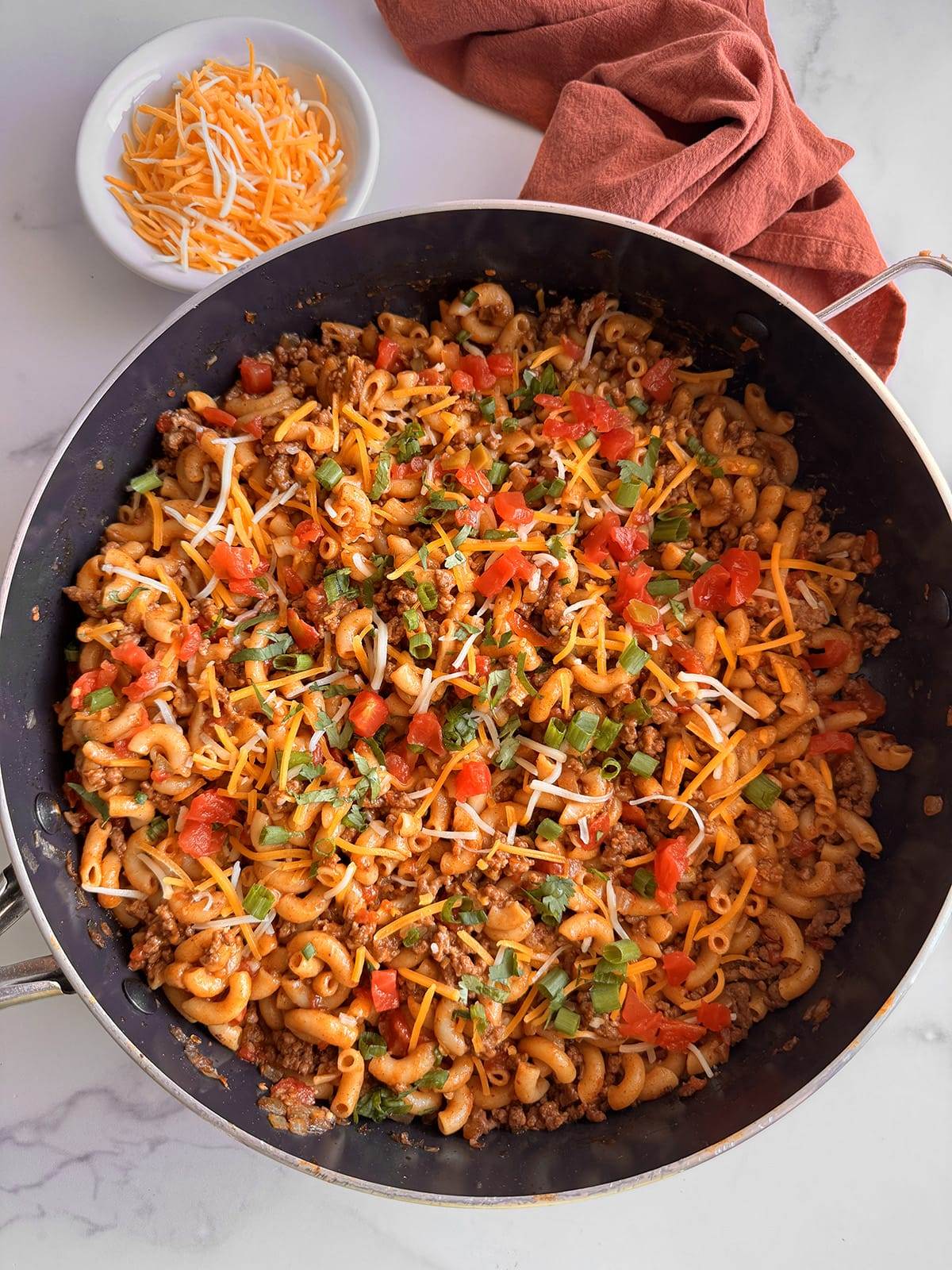 A skillet full of taco pasts topped with cheese and herbs with a side of cheese.