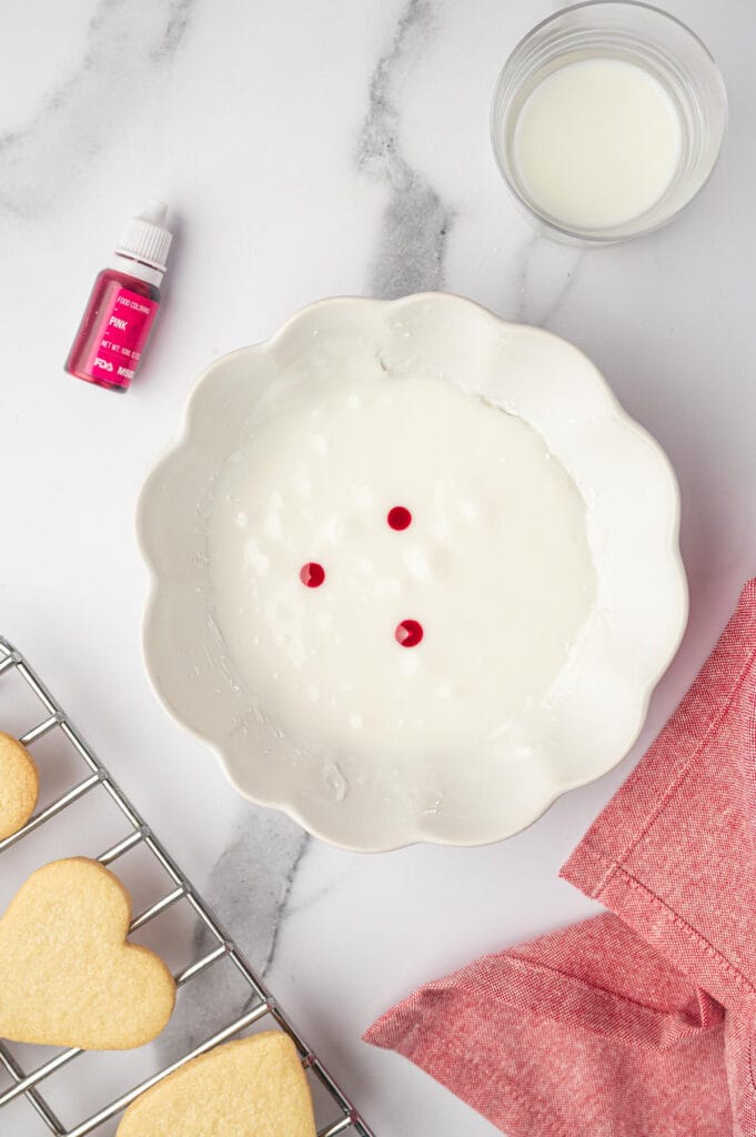 White frosting in a bowl with dots of food coloring for heart-shaped sugar cookies recipe.