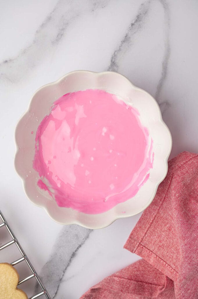 A bowl of pink frosting for heart-shaped sugar cookies recipe.