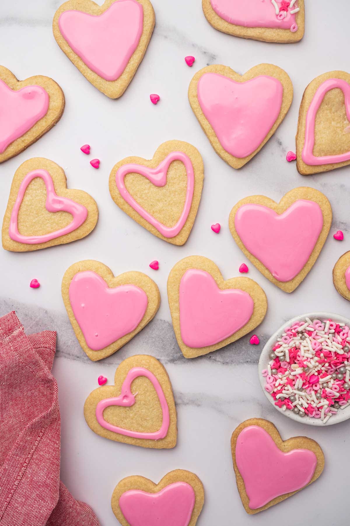 Heart-shaped sugar cookies over a white tablecloth with a bowl of sprinkles.