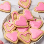 A plate of heart-shaped sugar cookies with pink frosting.