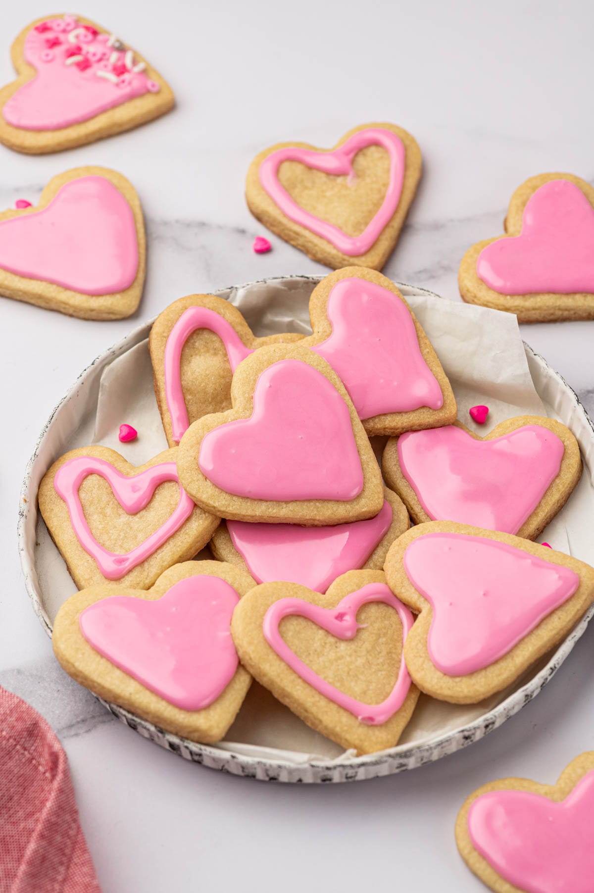 A plate of heart-shaped sugar cookies with pink frosting.