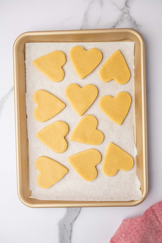 Heart-shaped sugar cookies on a baking dish with parchment paper before going in the oven.