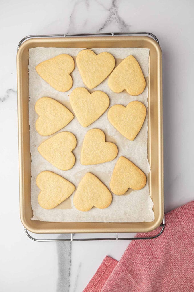 Freshly baked heart-shaped sugar cookies on a cookie sheet with parchment paper.