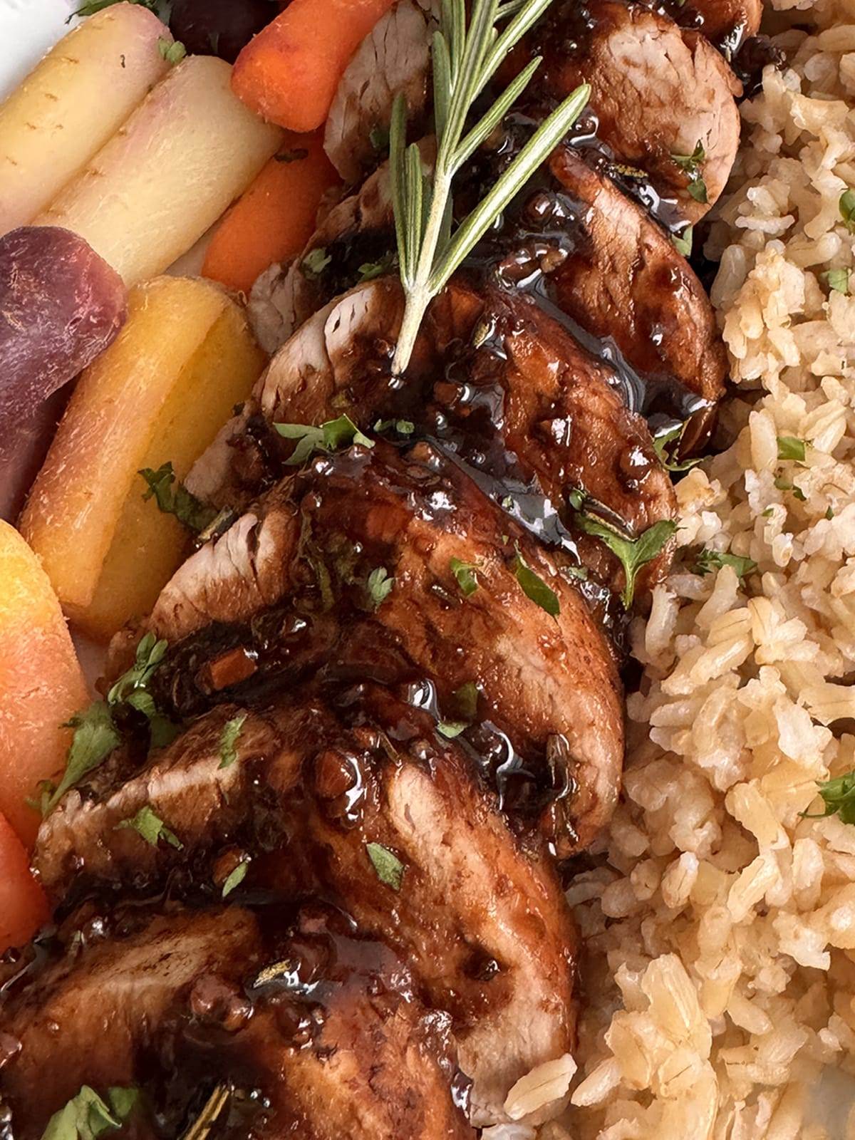 A plate with balsamic pork tenderloin, brown rice and carrots.