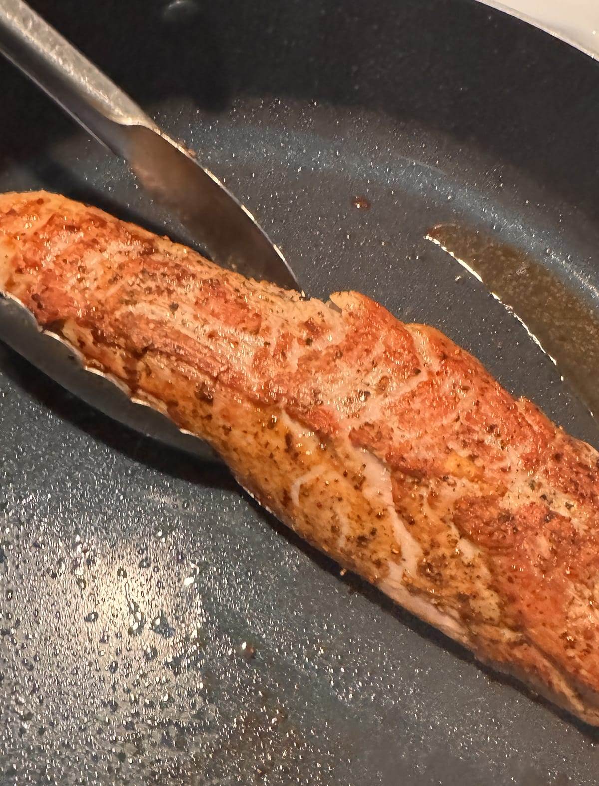 Browning a pork tenderloin in a skillet.