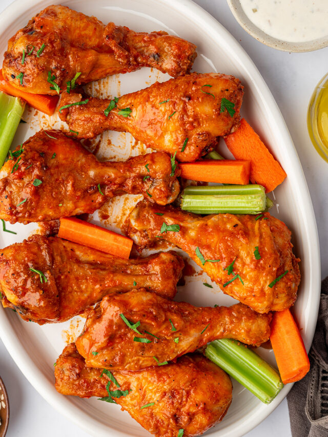 Buffalo baked chicken legs on a serving dish with celery and carrot sticks.