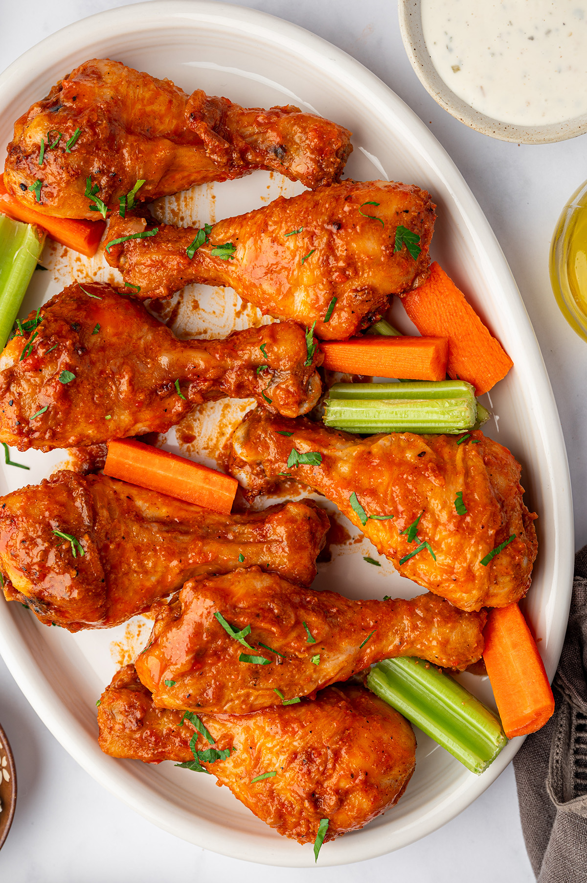 Buffalo baked chicken legs on a serving dish with celery and carrot sticks.