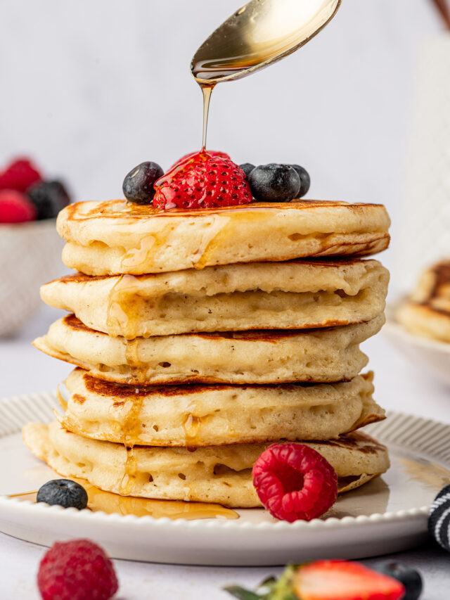 A stack of classic buttermilk pancakes with berries and maple syrup.