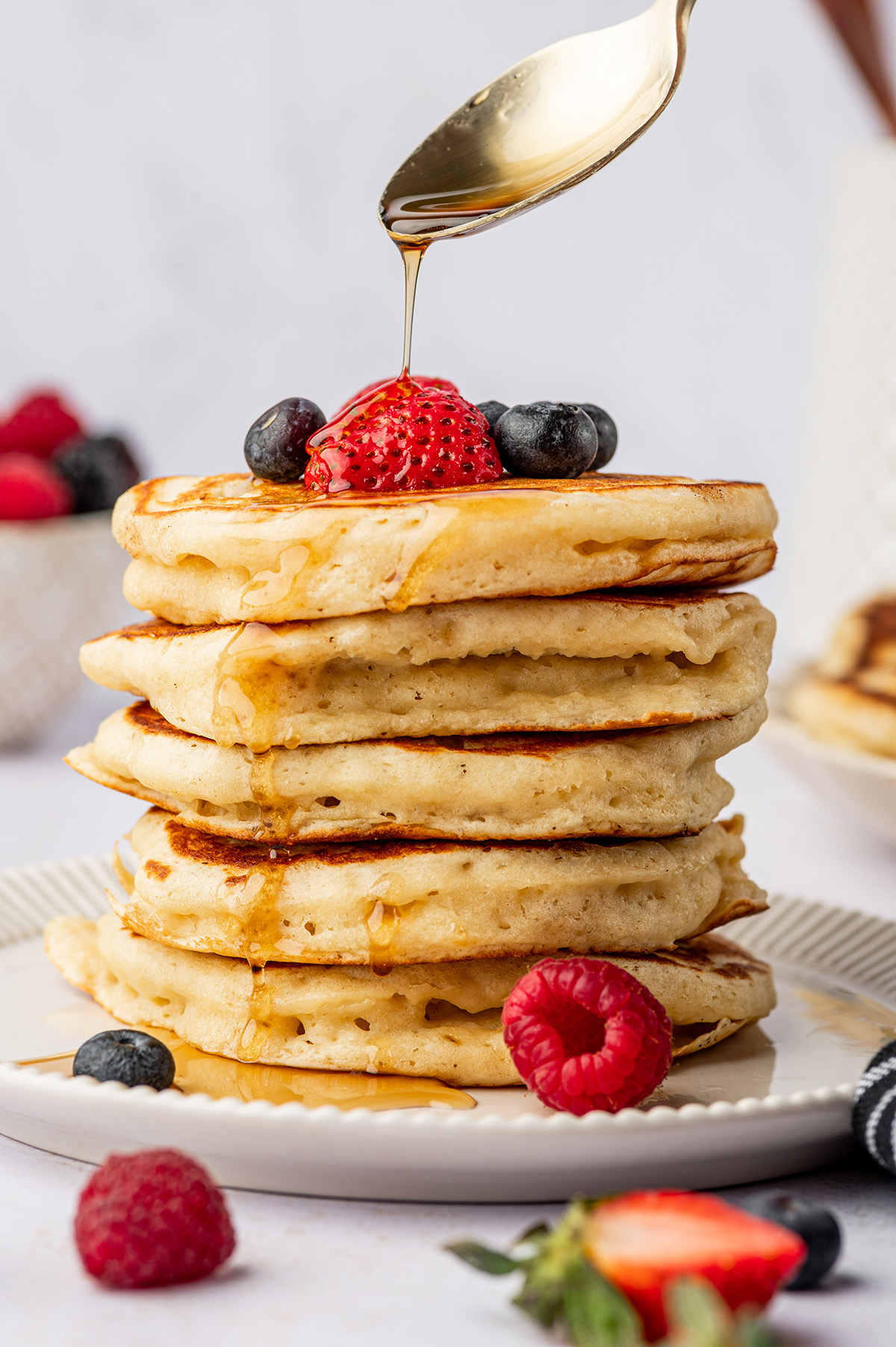 A stack of classic buttermilk pancakes with berries and maple syrup.
