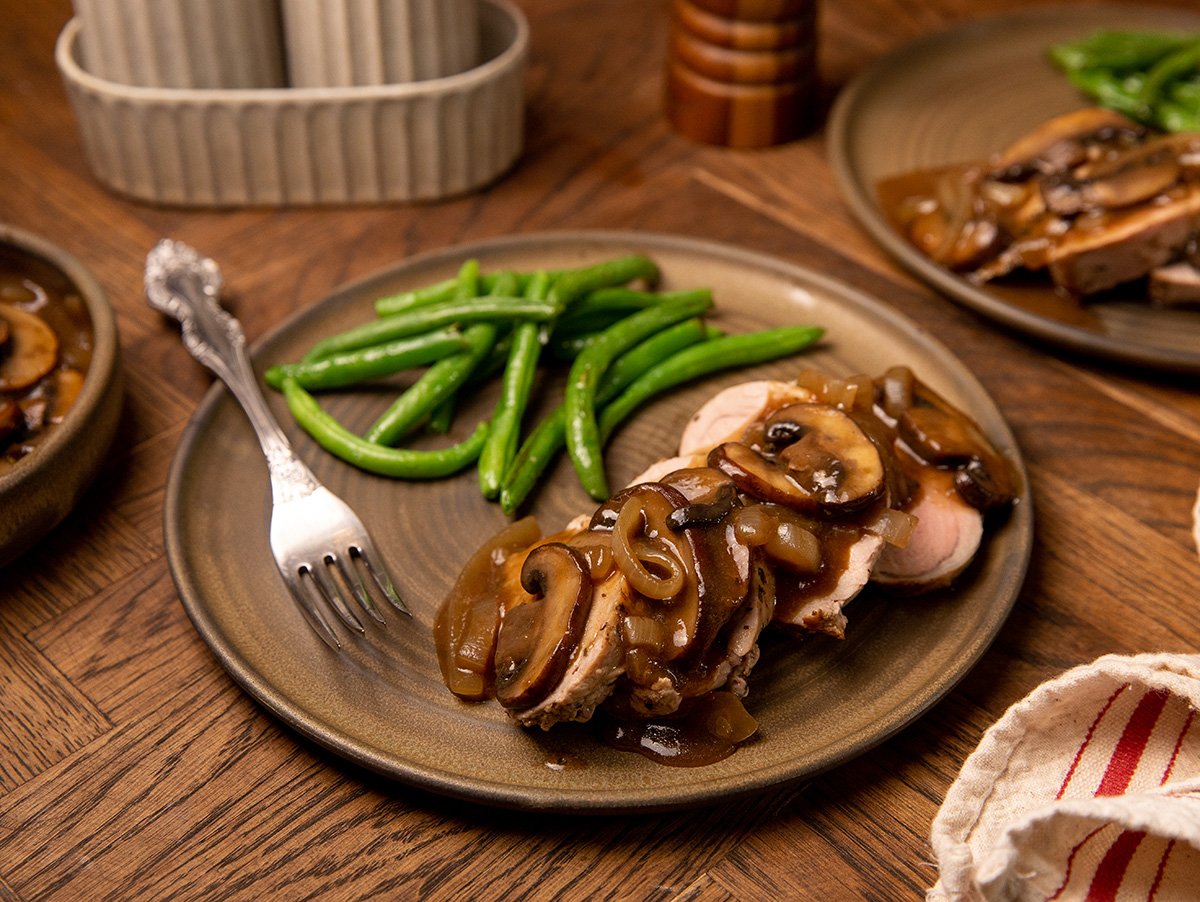 Smothered pork tenderloin on a brown plate with green beans.