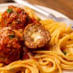 Close up of cheesy stuffed meatballs over spaghetti noodles.