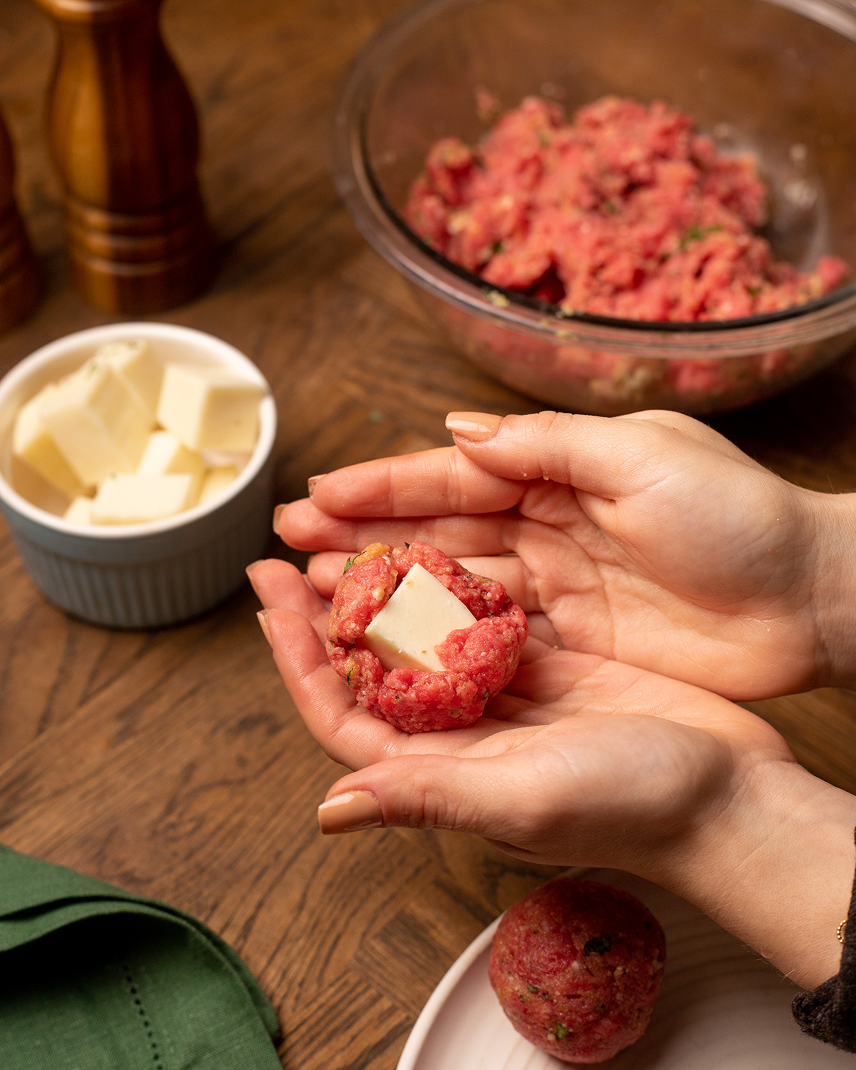 Adding a cube of mozzarella into ground beef to make stuffed meatballs.