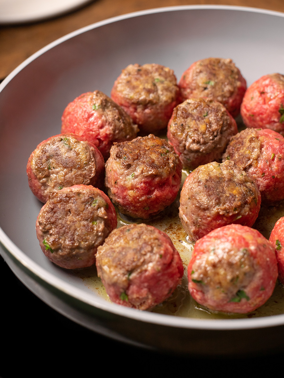 Stuffed meatballs browning in a gray skillet.