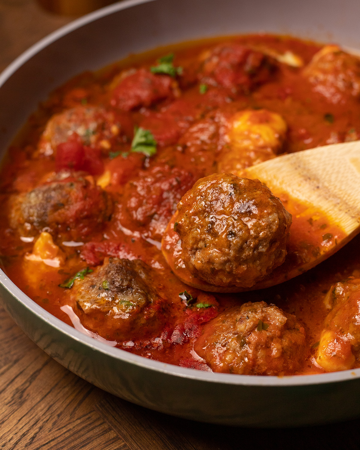 Stuffed meatballs simmering in a skillet with a wooden spoon.