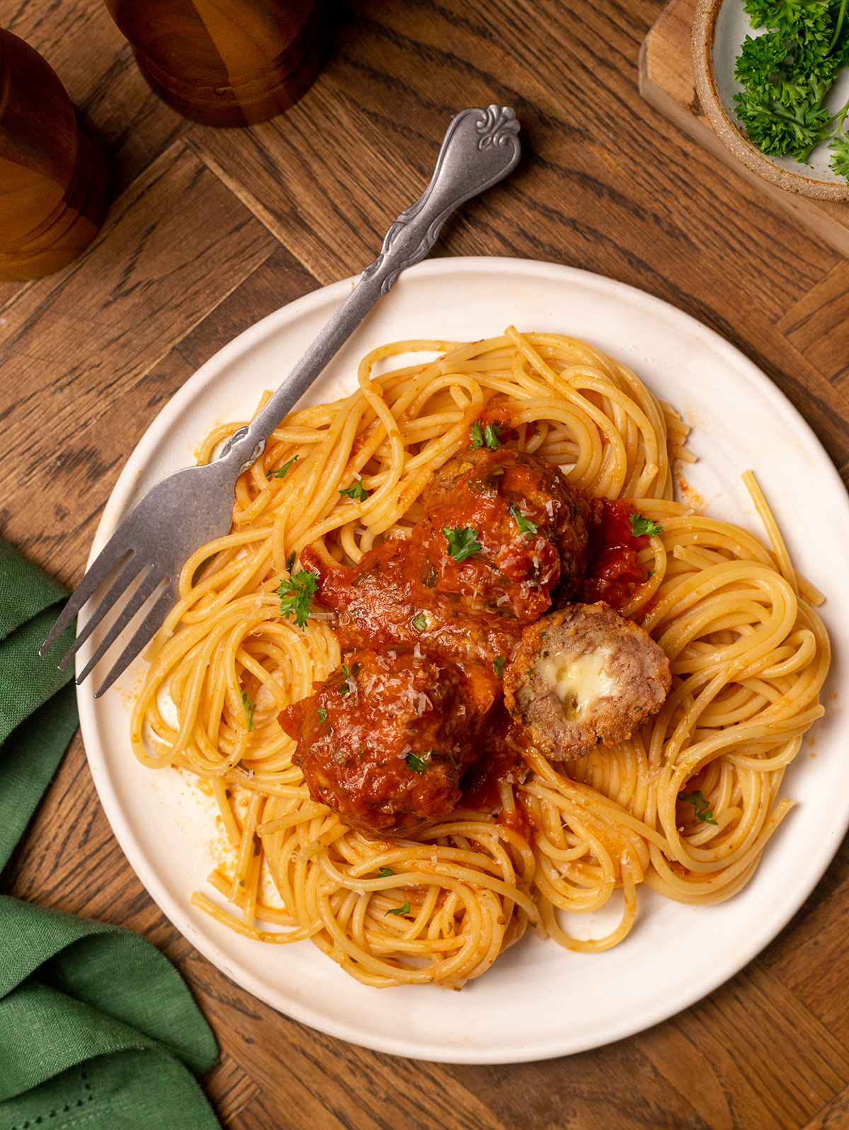A hero shot of cheesy stuffed meatballs over spaghetti noodles on a white plate.