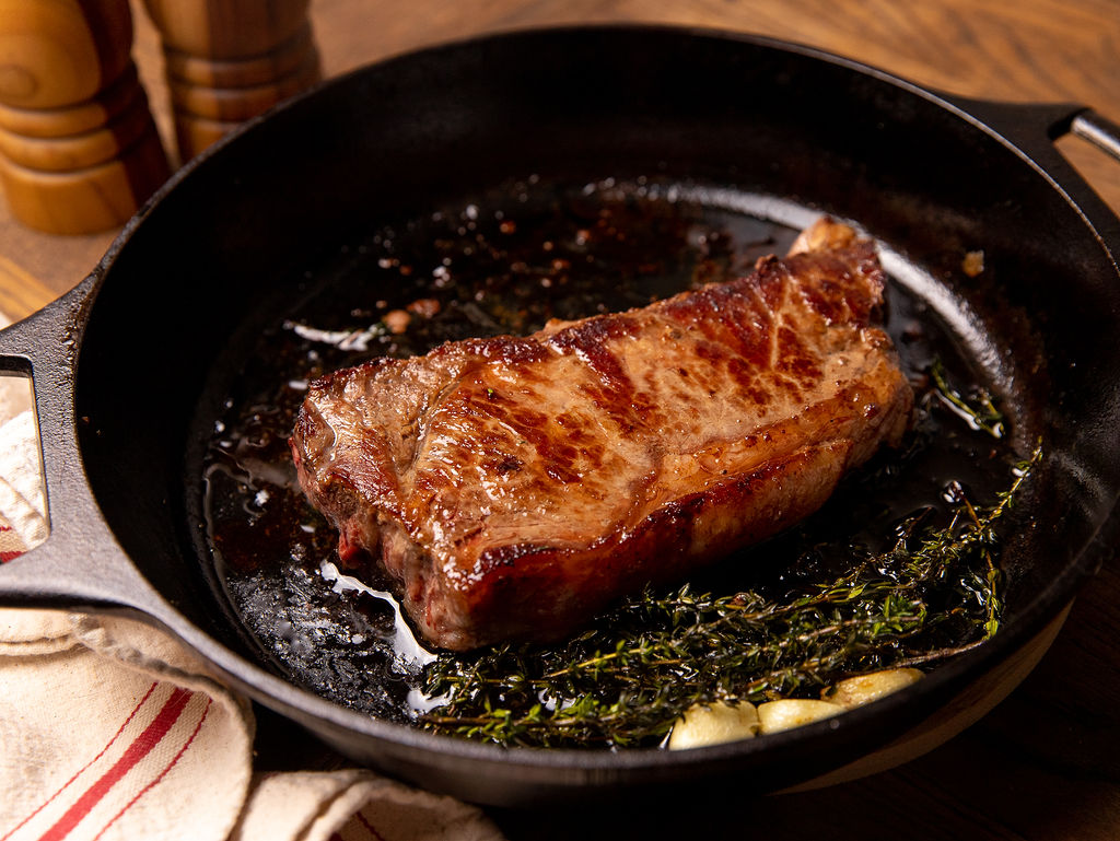 A juicy steak cooking in a cast iron pan with butter and garlic.