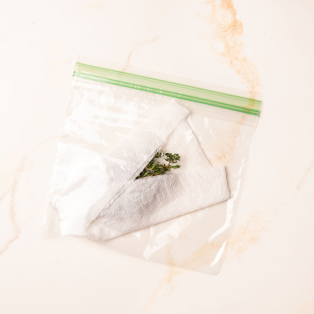 Fresh herbs stored in a plastic bag covered in paper towel.