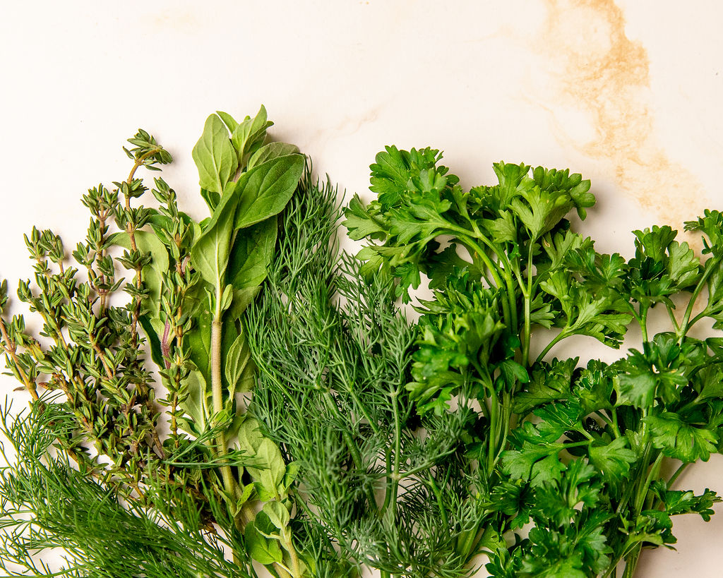 An assortment of fresh herbs on a cream colored marble surface.