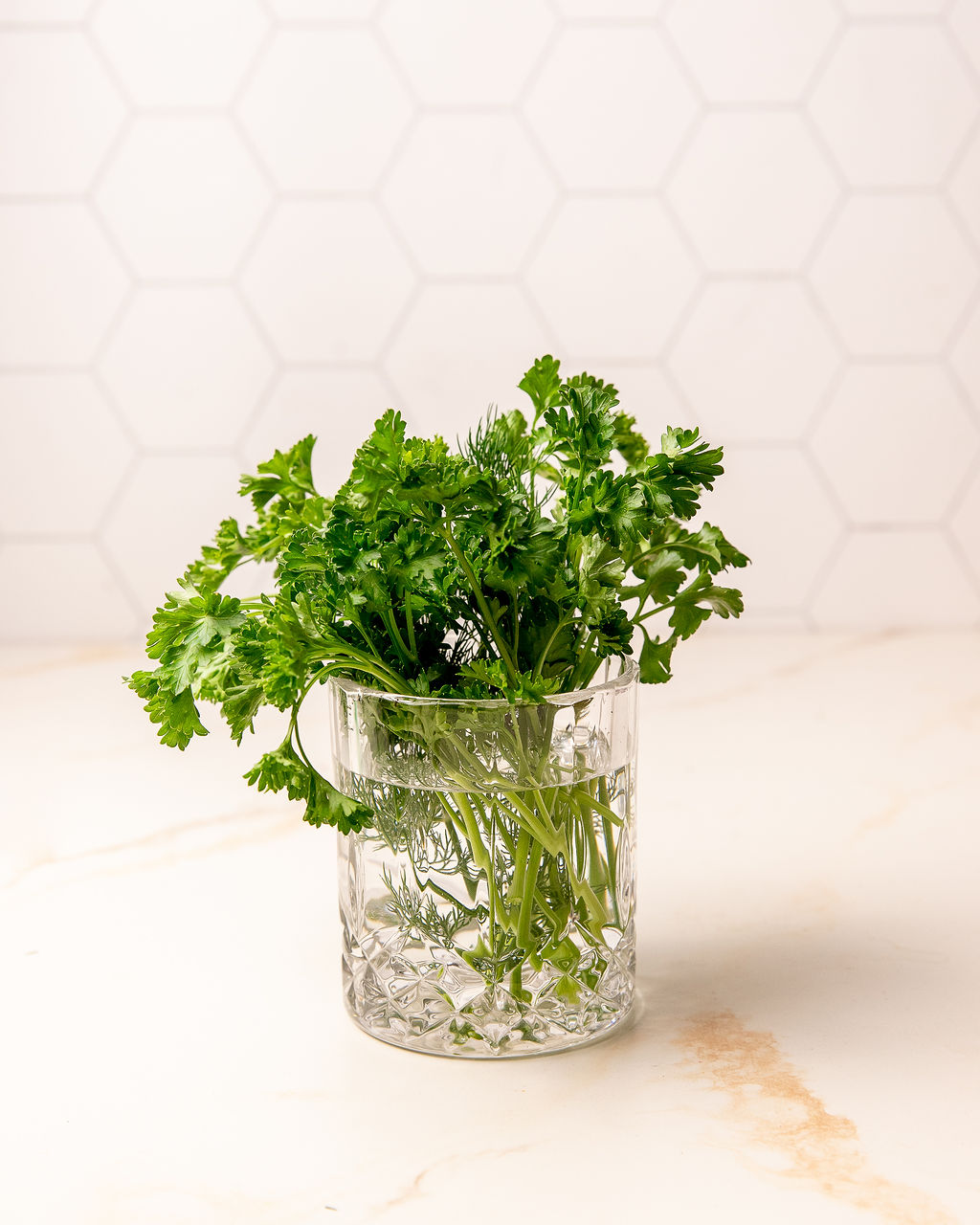 Parsley in a glass jar in front of a cream colored backdrop.
