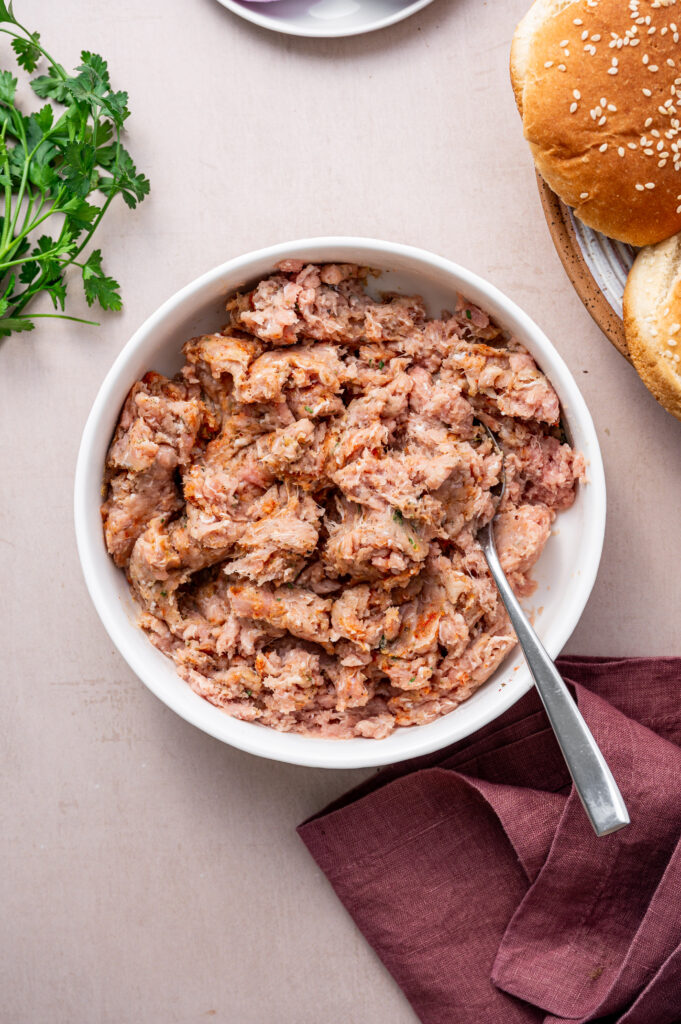 Mixing the spice mix with the ground turkey in a white bowl.