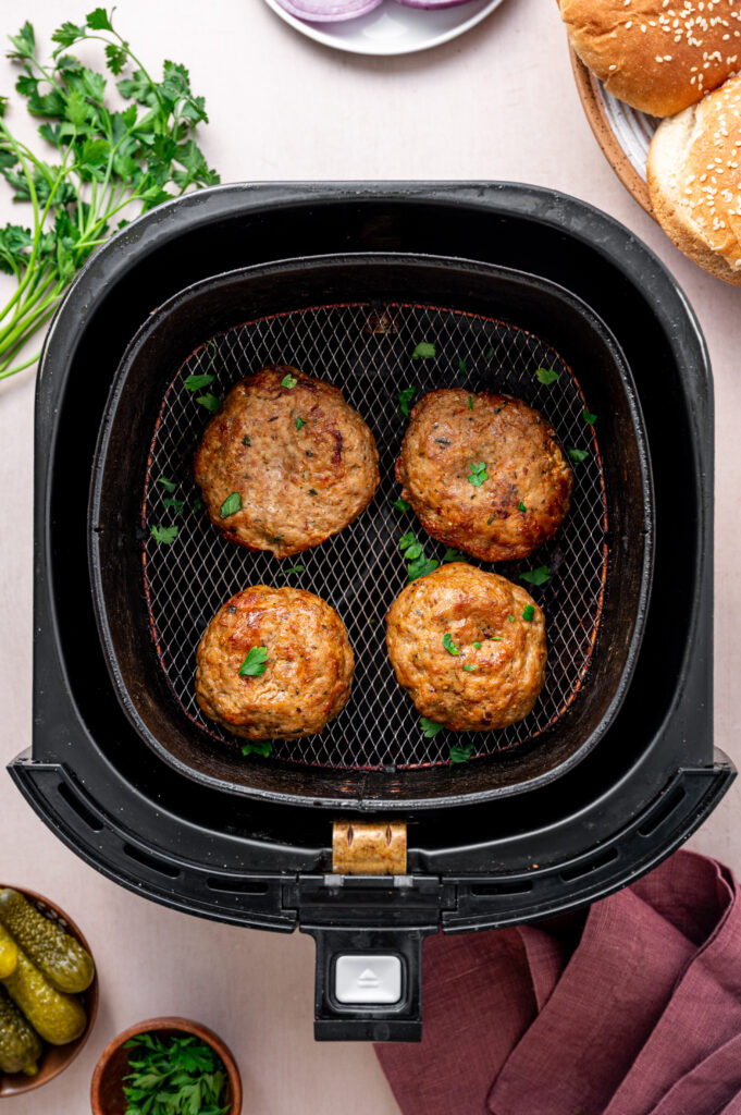 Four turkey burger perfectly cooked in an air fryer basket with a fresh herb garnish.