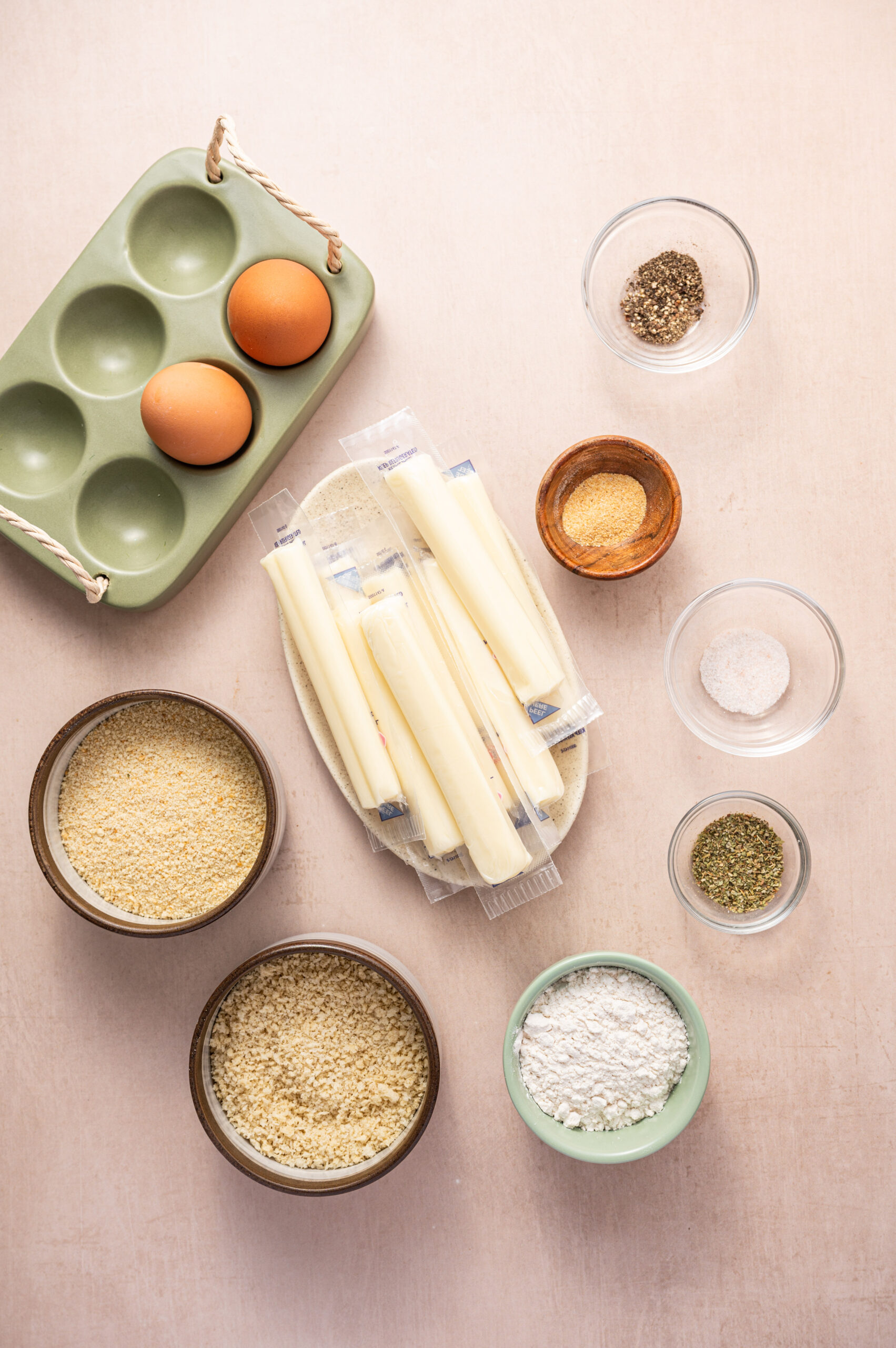 Ingredients for air fryer mozzarella sticks on a light pink surface.