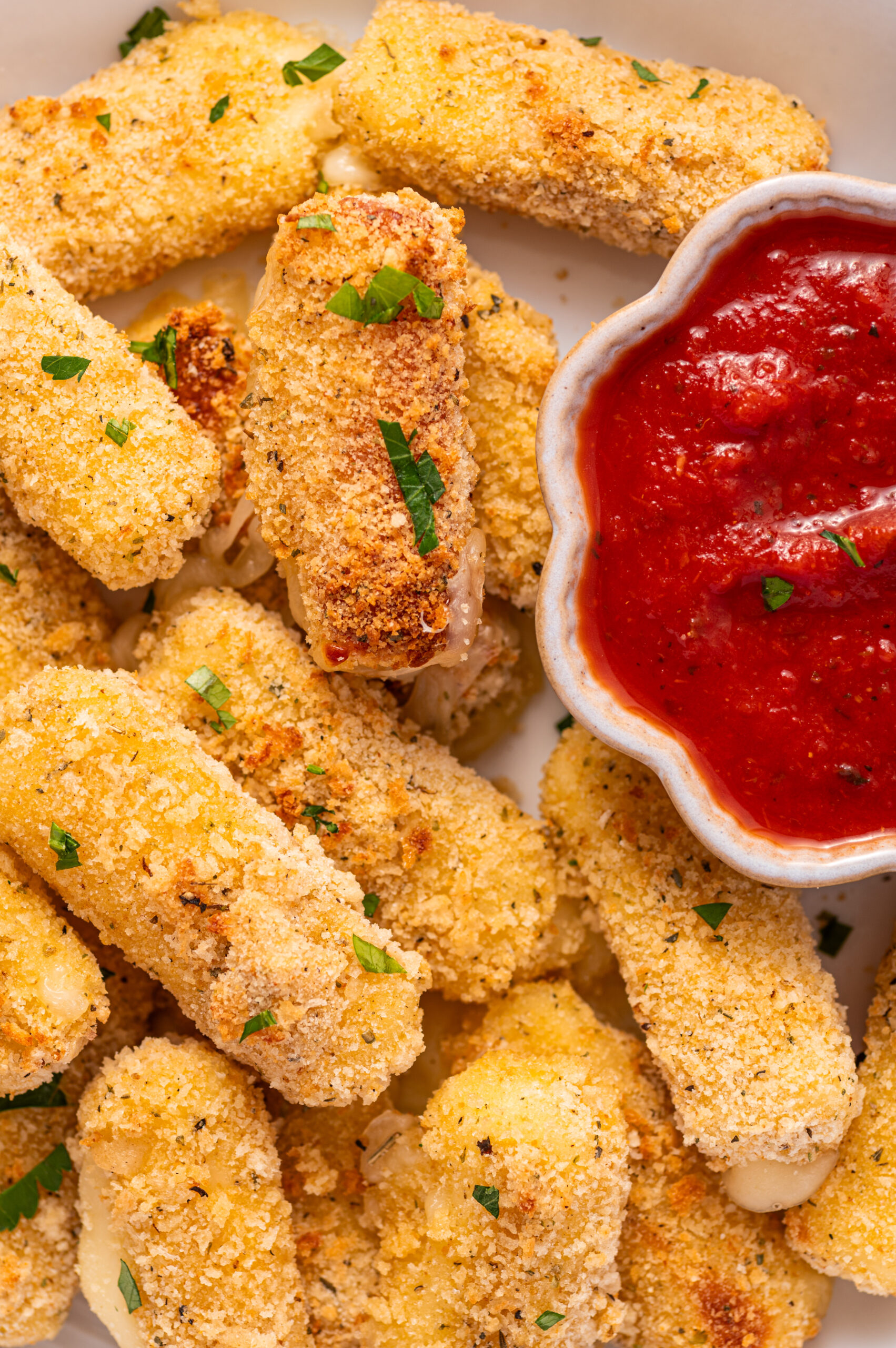 Close-up of air fryer mozzarella sticks in a bowl with marinara dipping sauce.