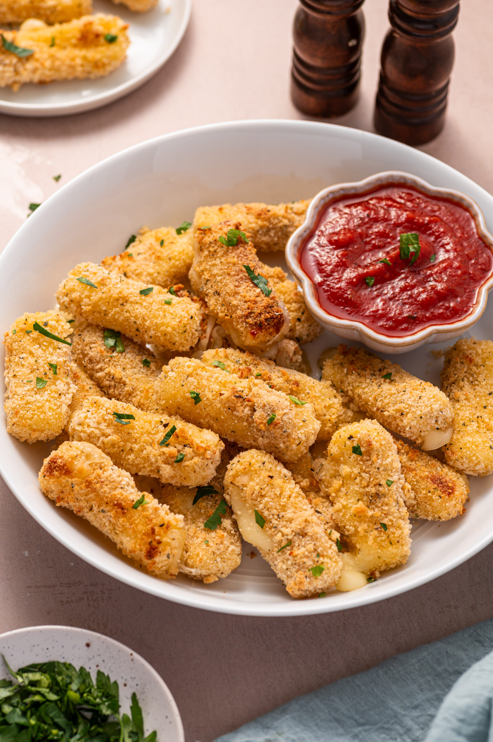 Air fryer mozzarella sticks in a white bowl with marinara dipping sauce on the side.