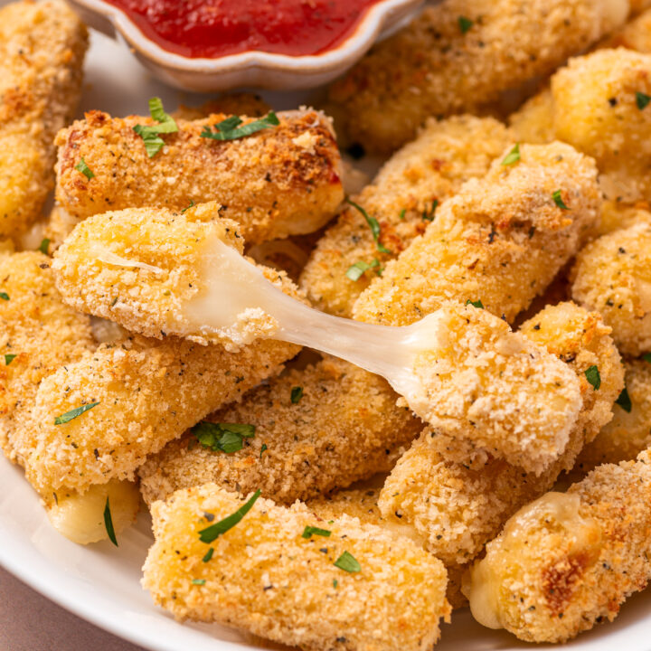 A pile of air fryer mozzarella sticks with one stick showcasing it's gooey cheese pull.