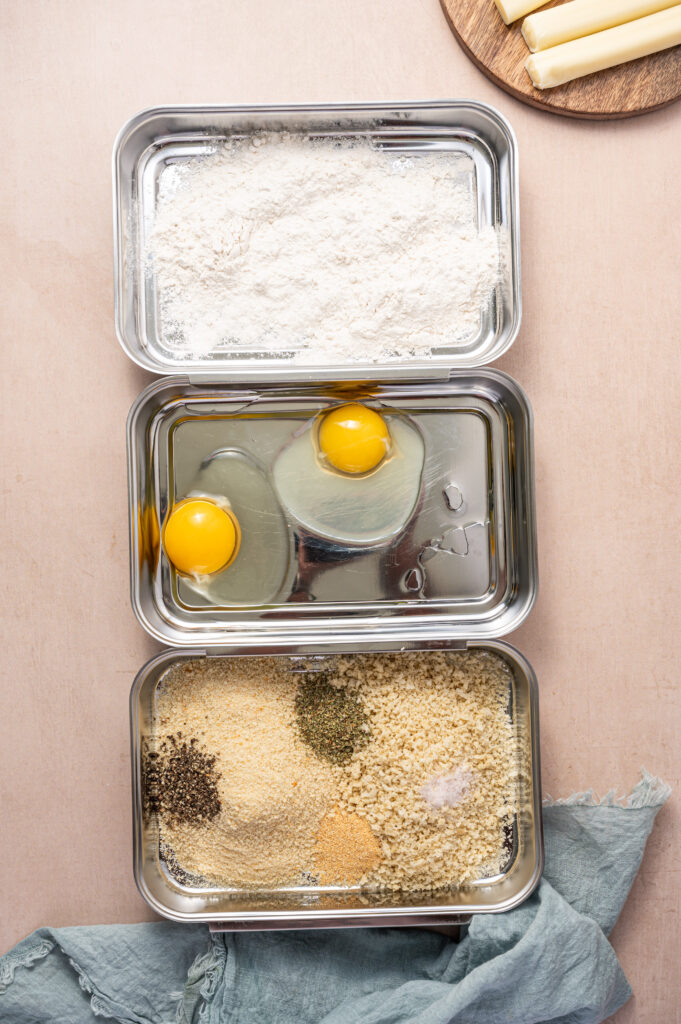 The breading station for air fryer mozzarella sticks, showing a dish for flour, eggs, and breadcrumbs.