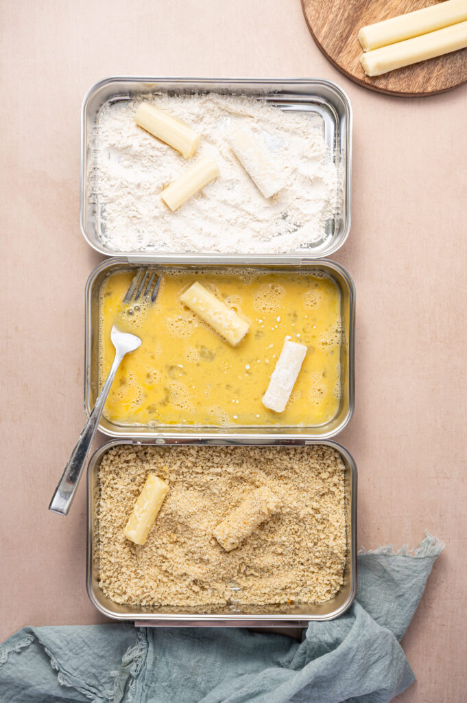 Air fryer mozzarella sticks getting coated in flour, eggs, and breadcrumbs.
