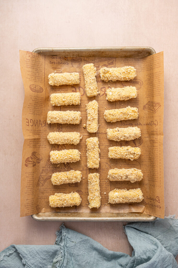 Mozzarella sticks on a baking sheet ready to get placed in an air fryer.