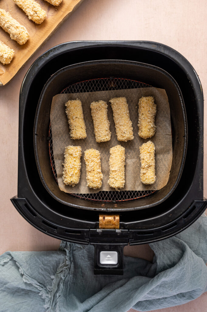 Mozzarella sticks in an air fryer basket getting ready to cook.