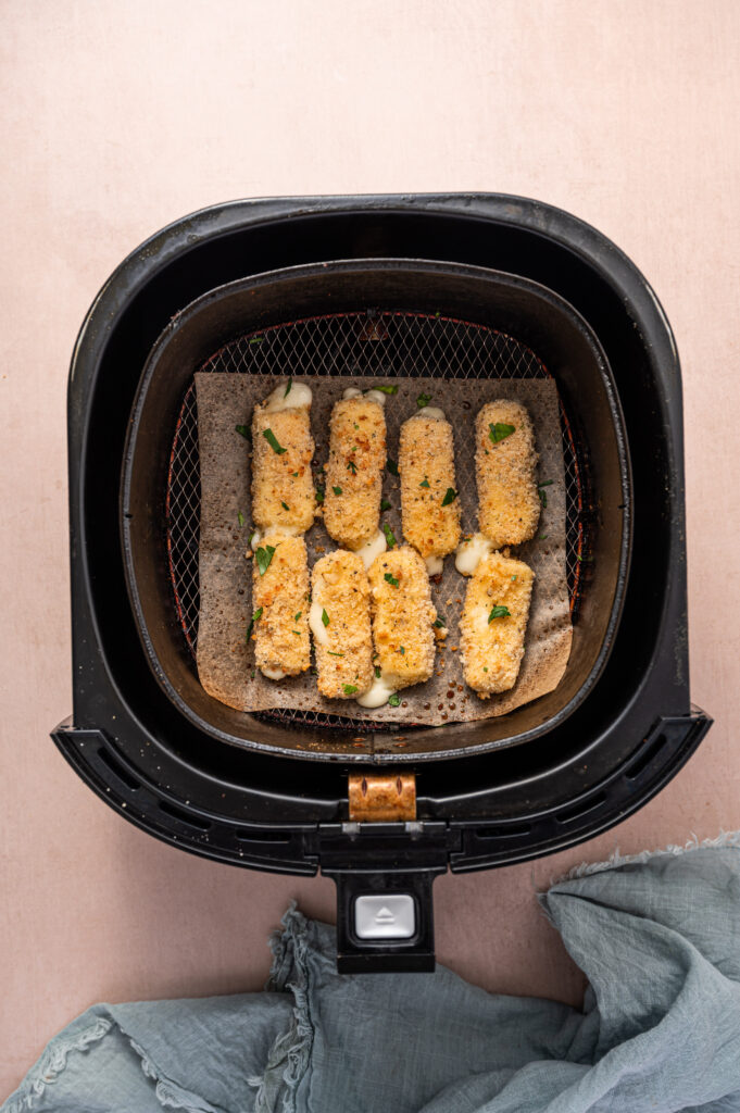Perfectly golden and crispy air fryer mozzarella sticks in an air fryer basket.