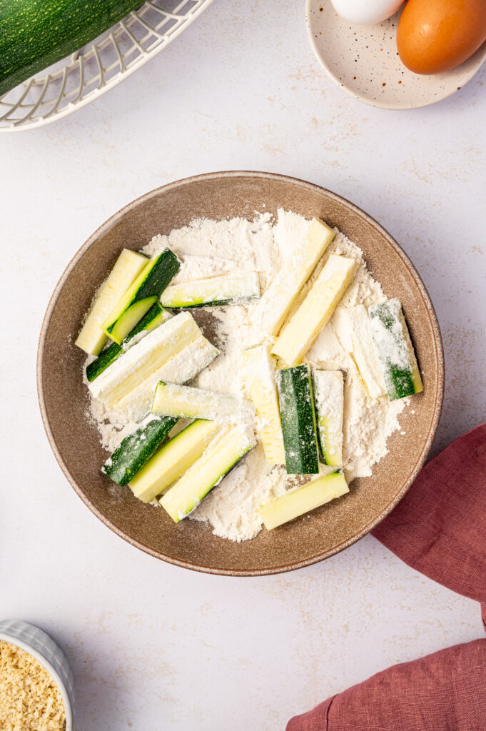 Zucchini sticks in a bowl of flour.