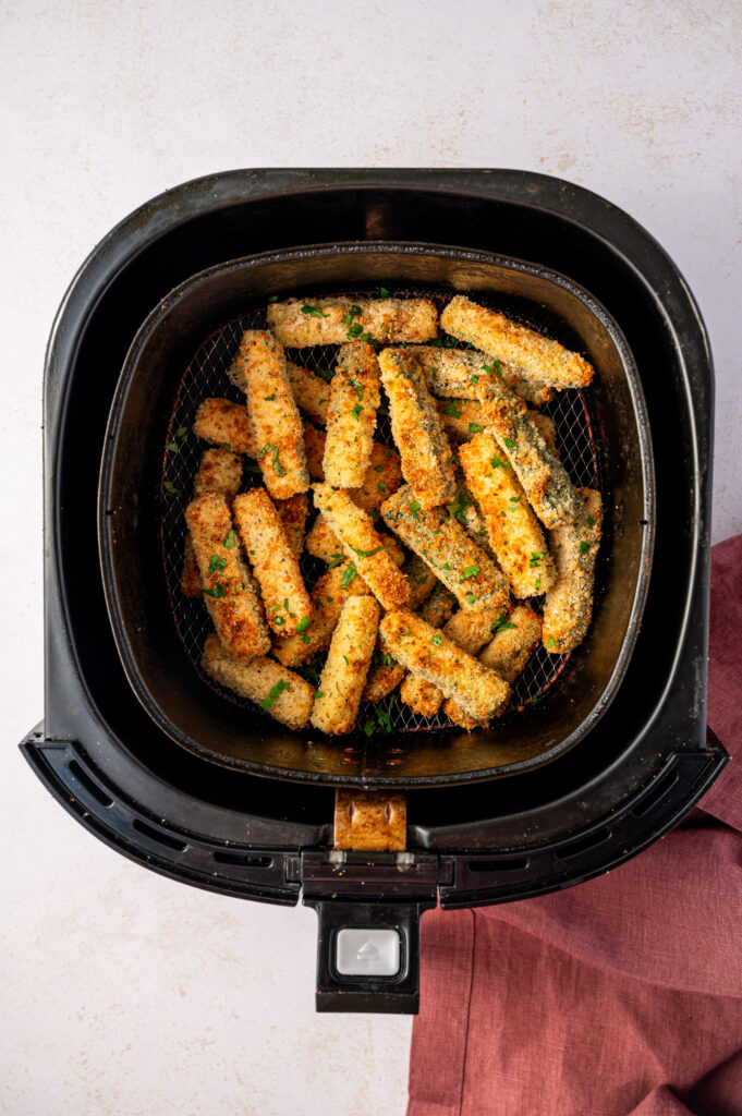 Air fryer zucchini fries in an air fryer basket ready to eat.
