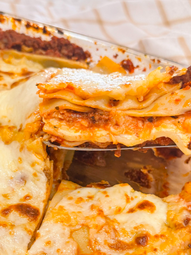 A close-up of a slice of oven baked lasagna being lifted from a glass baking dish, showing layers of pasta, meat sauce, and melted cheese.