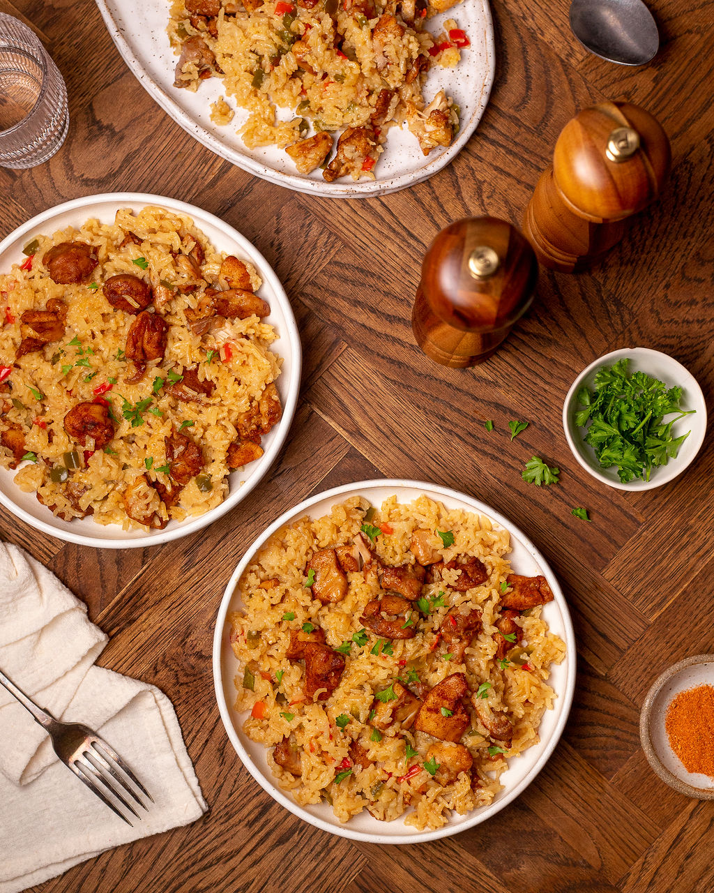 White bowls of Cajun chicken and rice on a wooden surface with salt and pepper shakers.
