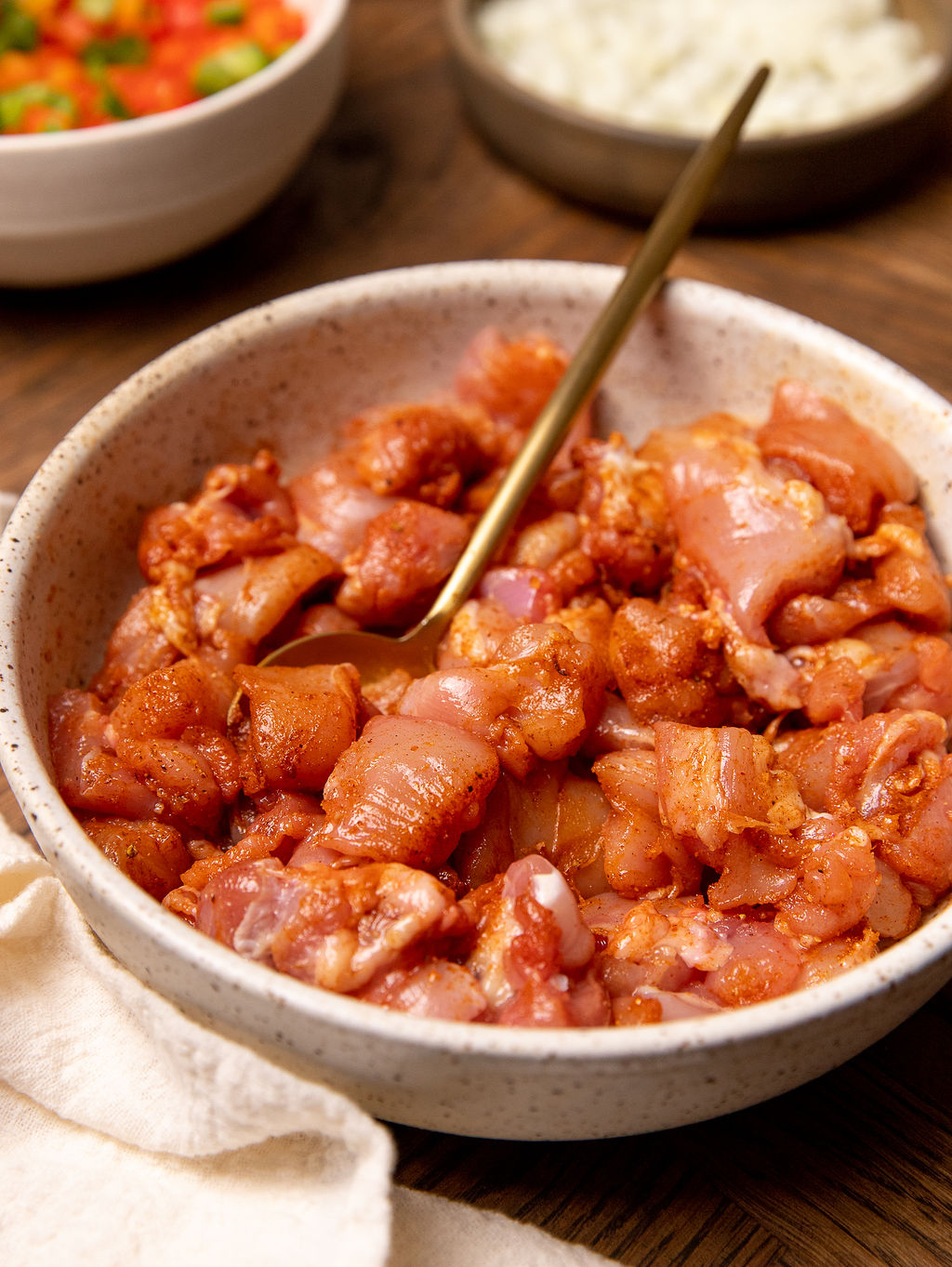 Adding seasoning to chicken thighs in a white bowl.