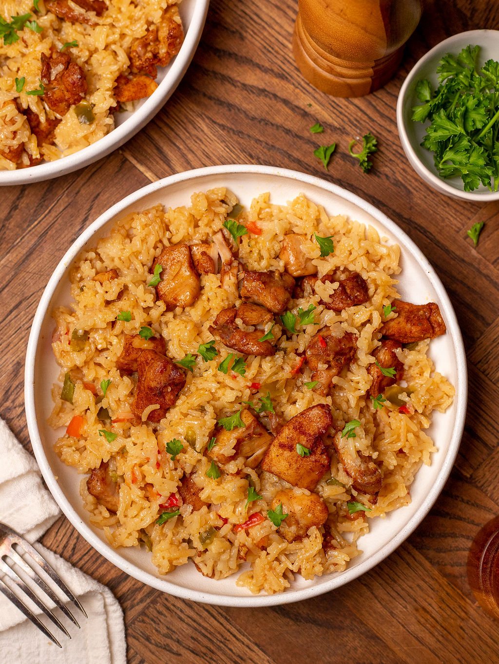 A serving of Cajun chicken and rice in a white bowl over a wooden surface.