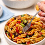 Dipping a fork into a white bowl of colorful cowboy caviar pasta salad.
