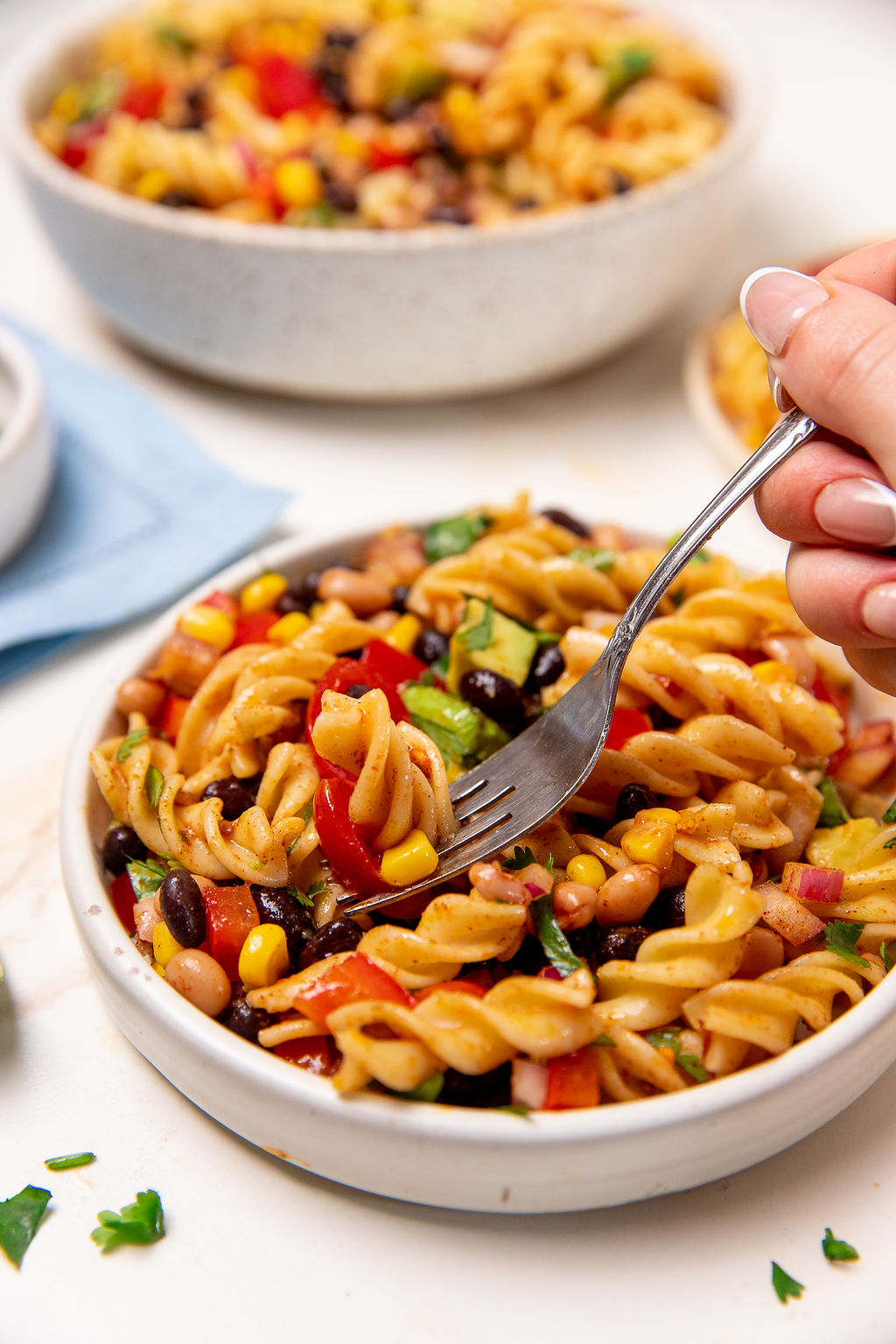Dipping a fork into a white bowl of colorful cowboy caviar pasta salad.