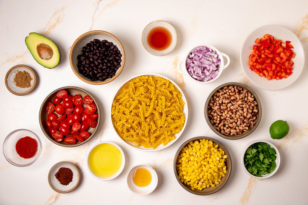 All the ingredients to make cowboy caviar pasta salad on a white counter top.