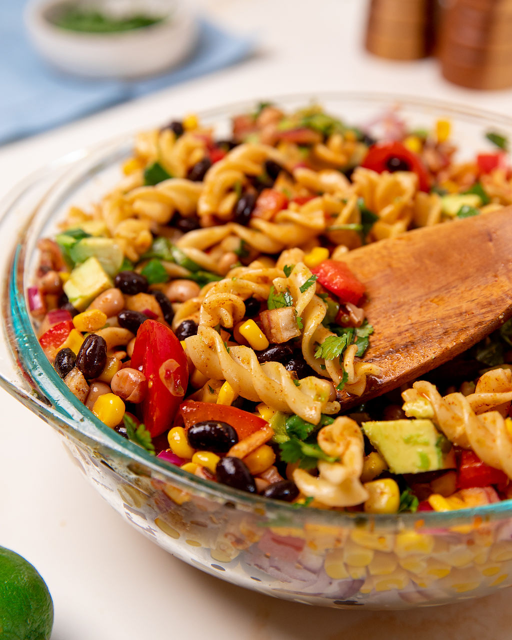 Close-up of cowboy caviar pasta salad in a glass bowl with a wooden spoon dipped in.