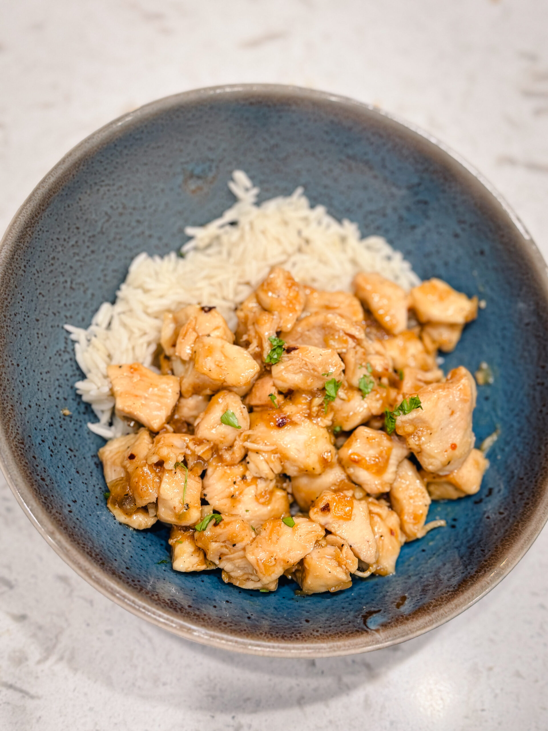 Honey garlic chicken on a blue plate with white rice.