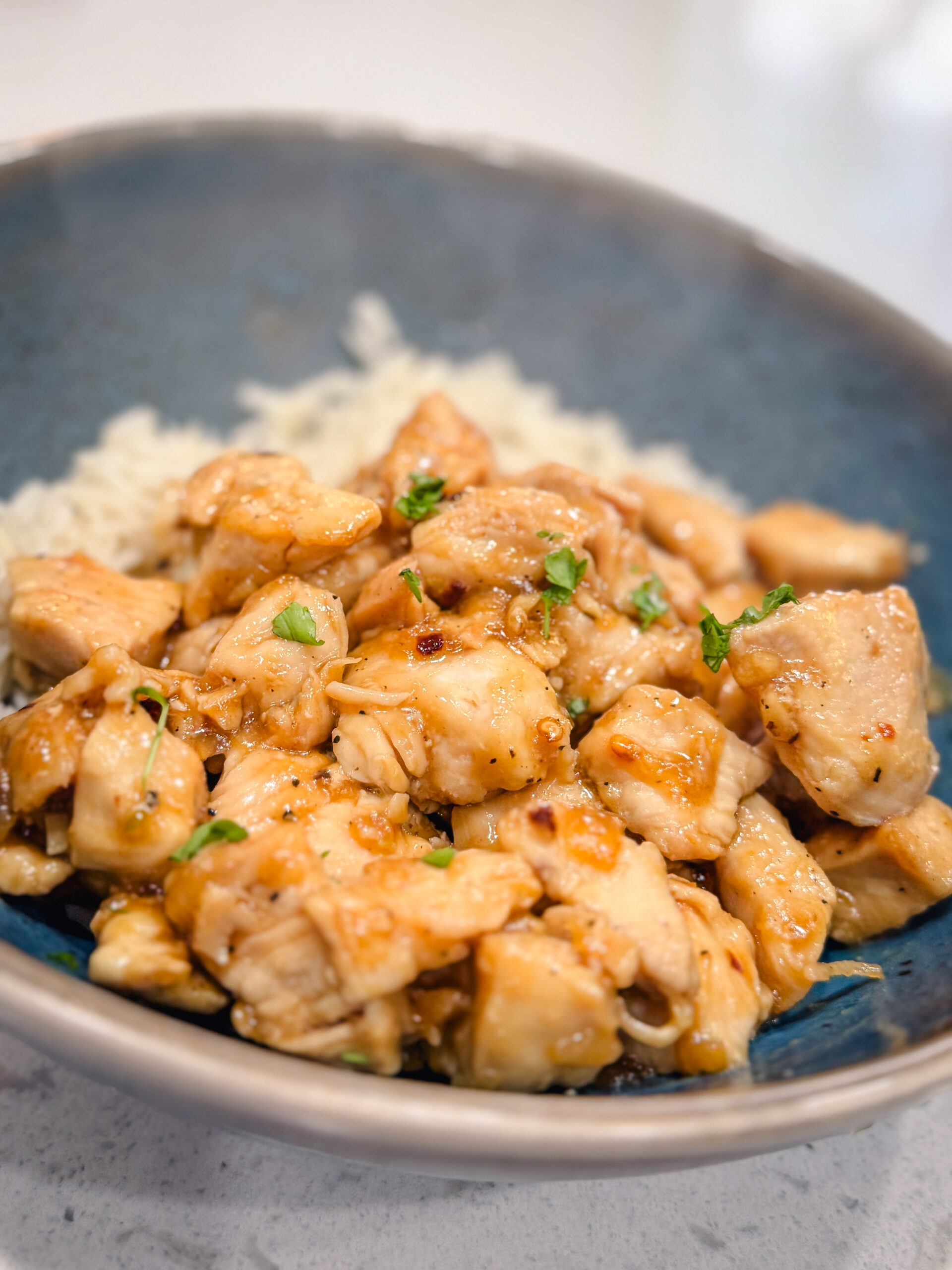 Close-up of steamy honey garlic chicken on a blue plate with white rice.