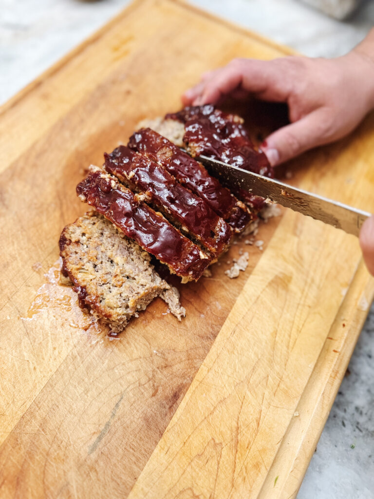 Cutting into a delicious classic homestyle meatloaf over a wooden cutting board.