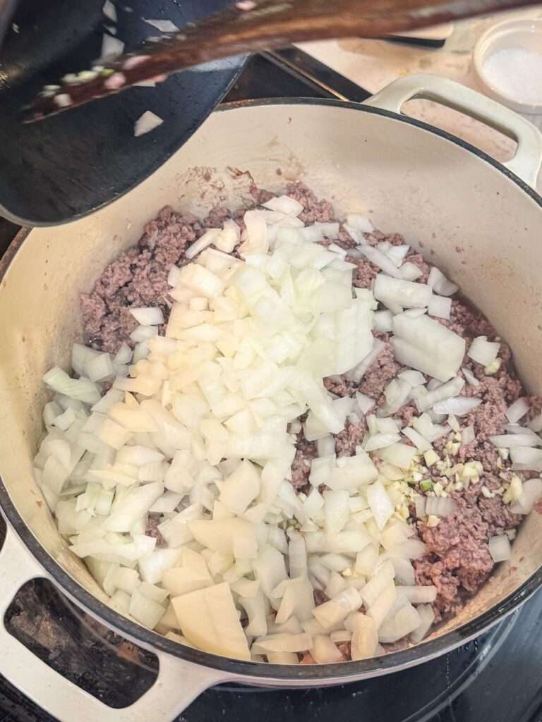 Adding onions to Dutch oven with the browned beef.