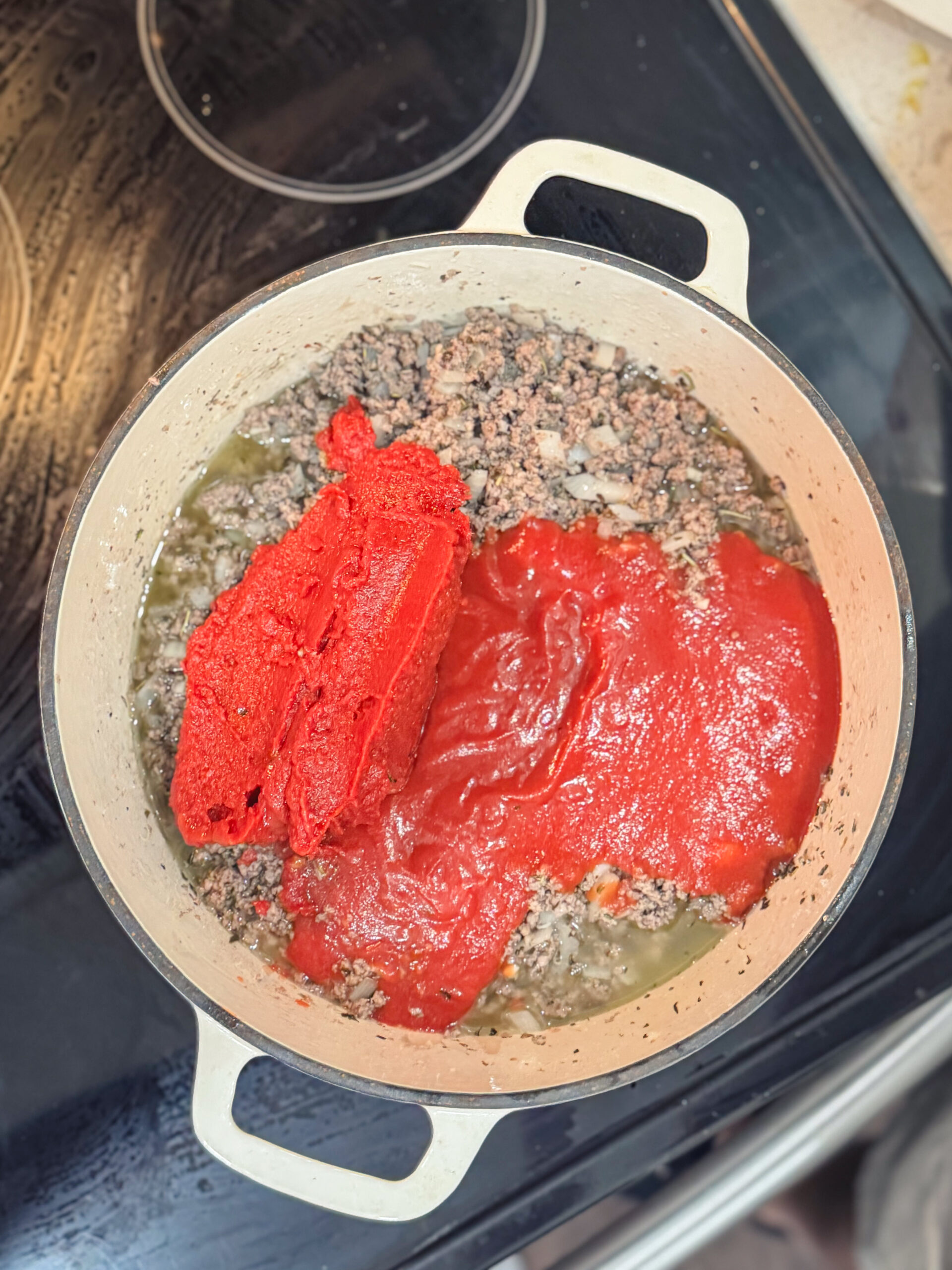 Adding tomato paste and sauce in a Dutch oven full of browned beef.